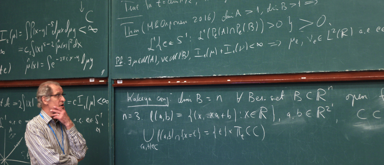 Kuva SMYn 150-vuotisjuhlista. Matemaatikko täyden liitutaulun edessä pohtimassa.