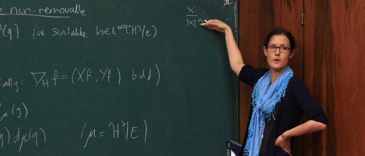 Kuva SMYn 150-vuotisjuhlista. Matemaatikko liitutaulun vieressä esitelmöimässä.