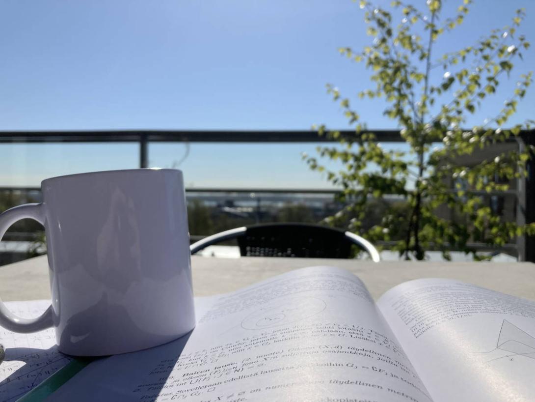 Avoin topologian oppikirja, taustalla koivu kesäisellä parvekkeella.